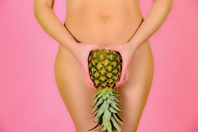 Frau hält sich eine umgedrehte Ananas vor ihren Intimbereich