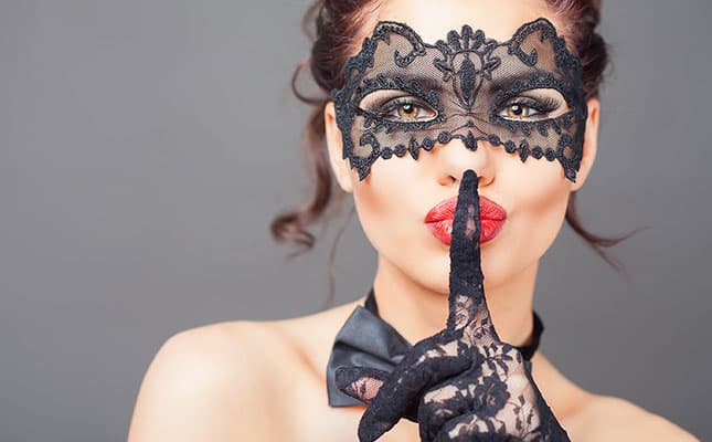 Frau mit Karneval Maske hält sich ihren Finger vor den Mund